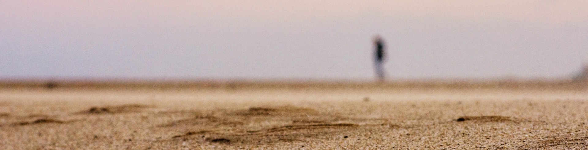 A man is standing in a desert landscape. He is on the horizon and his shape is blurred by the heat haze.
